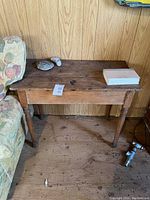 Small rectangular wooden table with visible surface wear, positioned next to floral upholstery and wood panel wall.