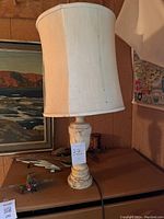 Photo of a stone lamp with a heavy stone base and white fabric shade placed on a table with other items in the background.