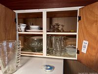 Wide shot of cabinet contents showing various glassware and ceramic items on shelves, including pitcher, punch bowl, plates, and teacups.