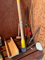 Tools arranged on wood shelves showing pickaxe, red handled hedge trimmers, mitre box, pipe wrench, mallet