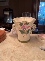 Photo of a white porcelain vase with scalloped top edge, double scroll handles and floral painted design on front.