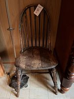 Front view of a vintage wooden chair showing the rounded spindle backrest, solid wooden seat, and four turned legs. The chair has visible wear and aged wood patina.