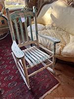 Front angle view of wooden rocking chair showing slatted seat and backrest with distressed white paint.