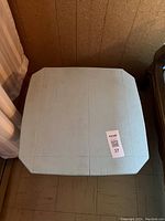 Top view of a square blue wooden side table with visible surface lines and some wear, placed between a fabric item and a wooden chair.