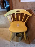 Yellow wooden chair shown from front angle. Chair has spindle backrest and carved legs. Minor surface wear visible.