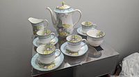 Photo showing the entire tea set including teapot, cups, saucers, cream jug, and sugar bowl on reflective surface.