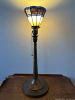 Full view of the antique cast-iron torchiere lamp illuminated, showing overall height and base design.