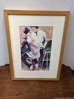 Framed figural watercolour painting showing two figures sitting with backs facing the viewer, painted in abstract-expressionist style with soft pastel colors and natural wood frame.