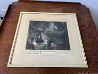 Framed coloured engraving titled "The Bathers" resting on a wooden surface, natural light. Detailed artwork showing bathers in nature, mat and frame visible.