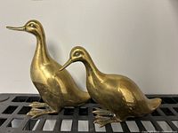 Pair of brass duck and goose sculptures on black surface showing their profile and size proportion.