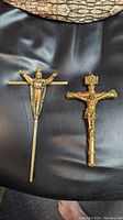 Photo showing two vintage gilt metal crucifix wall hangings lying on a black surface, highlighting their detailed design and gold-tone finish.