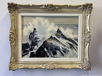 Frontal view of the rugged coastline oil painting with ornate cream-colored wood frame showing detailed crashing waves on rocks.