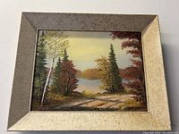 Front view of framed scenic lakeside oil painting with autumn trees and lake, signed Anna Jalava.