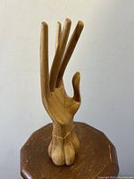 Front view of slender carved wooden hand sculpture with fingers extended and slightly bent, placed on a wooden surface.