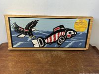 Front of the wooden box showing the Inuit style artwork on the lid with an eagle and animal under a yellow sun, signed Clarence A. Wells.