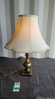 Desk lamp on black surface with visible brass base and cream fabric scalloped shade.