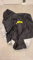 Full view of folded black and silver Rain-X motorcycle cover on tile floor, showing the overall fabric and colors