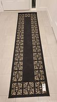 Photo showing the full length of the black hall runner with beige patterned border.