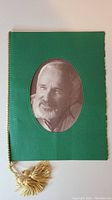 Front cover of the dinner program showing a green textured surface with an oval sepia portrait of Norman Jewison and a gold braid rope with tassels along the spine.