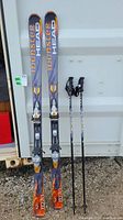 Pair of Head Monster M70 skis with diagonal bindings standing upright next to a pair of black Leki ski poles.