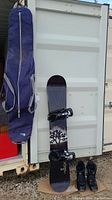 Full view of Ride Profile snowboard with bindings attached, boots in front, and snowboard bag hanging on the left side.