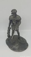 Front view of vintage pewter fur trapper figurine showing detailed attire, rifle, fur pelt, and base with snowshoes.