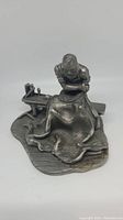 Front and side view of the pewter figurine depicting a man sewing sailcloth on a wooden deck base, positioned on a bench with tools nearby.
