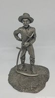Front view of the pewter figurine showing detailed farmer figure with hat, shirt, and scythe on textured base.