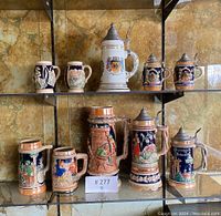 Front view of full set of 10 German beer steins arranged on glass shelves, showing detailed relief work and lids.