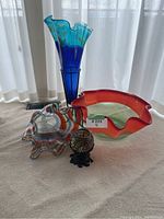 Front view of 3 blown glass decorative bowls and small vase on white cloth under soft natural light