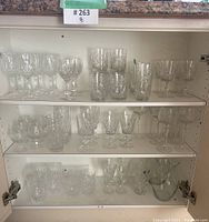 Full view of three cabinet shelves displaying varied crystal glassware and stemware including glasses, goblets, and two glass vases