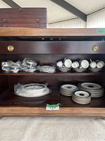Overall view of wooden serving hutch shelf with plates, bowls, wrapped platter and stacked cups and saucers.