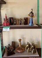 Overview of two shelves showing all lot items: St Basils replica, carved figurines, amber mugs, Russian ceramic figurine, glass decanter, brass horse bookends, and a model ship bookend.