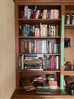 Full bookshelf showing many books stacked on four shelves along with boxed games and accessories on the desk below.