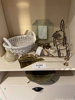 Shelf with white woven basket, small mirror, brass candle holders, brass scoop, decorative stand, and small ceramic decor items