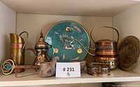 Shelf with various copper, brass, and Egyptian-themed decorative items including plates, pitchers, kettles, incense burner, and figurines.