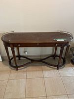 Front view of Lane console table showing wood finish, brass gallery rail, drawer with keyhole and pull, curved legs with stretcher base.