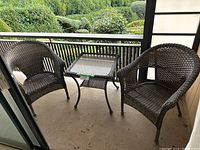 Patio set on balcony, includes square glass top table and two plastic rattan chairs spaced on each side of table