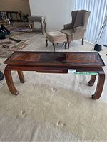 Front view of the dark wood sofa table with two inlaid art panels and curved legs, placed on carpet with adjacent armchair and ottoman in background.