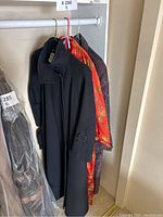 Three hanging garments including a black coat, red kimono, and patterned trench coat