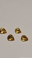 Four pear-shaped bright yellow sapphires arranged on a light background, showing clarity and cut.