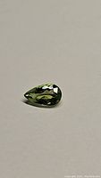 Pear cut mint green tourmaline gemstone placed on a plain surface, showing faceted top view and size proportions.