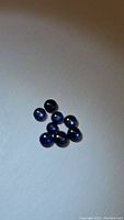 Eight small natural blue sapphire round cabochon gemstones displayed on a neutral background with visible reflections.
