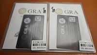 Two certification card sets with moissanite earrings displayed on top, indicating carat weight and certification details from GRA.