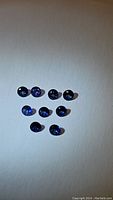 Nine faceted round blue sapphire gemstones of varying royal blue and cornflower blue color hues placed on white background.