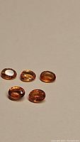 Close-up image showing five oval faceted Fanta Orange sapphires arranged on a plain background.
