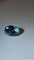 Oval cut lagoon blue zircon gemstone on a neutral background showing facets and color under light