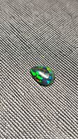 Close-up image of a pear-shaped black opal cabochon resting on a textured surface showing bright flashes of green, blue, and orange colors.