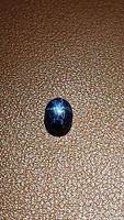 Photo showing natural blue star sapphire with 6-ray star, oval cabochon shape, taken on a textured brown surface.