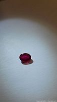 Photo of oval red ruby gemstone on white background, showing color and shape.